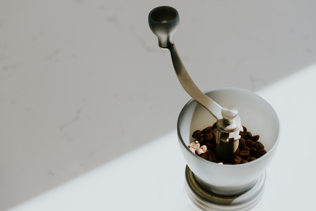 Overhead view of a manual coffee grinder's folding crank arm resting over a hopper filled with whole dark-roasted coffee beans
