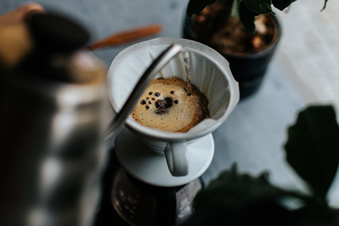 Hot water pouring from a gooseneck kettle into a paper-filtered pour-over dripper mid-bloom