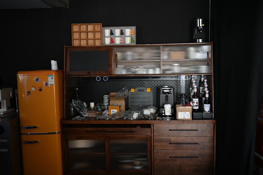 Orange refrigerator next to a wooden cabinet filled with items
