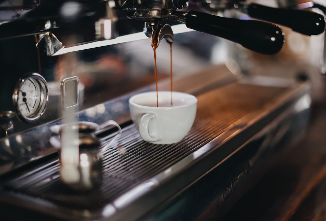 Espresso pouring in two dark streams from a portafilter into a small white cup on a commercial espresso machine