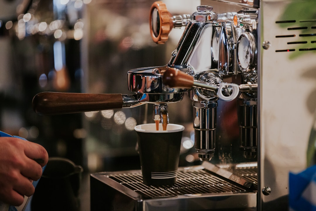 A barista's hand pulling a shot from a chrome portafilter espresso machine into a paper cup